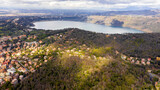 Aerial view of Lake Albano, a volcanic crater lake. A luxuriant forest grows around the water and on the left there is the city of Albano Laziale, in the Metropolitan City of Rome, Italy.