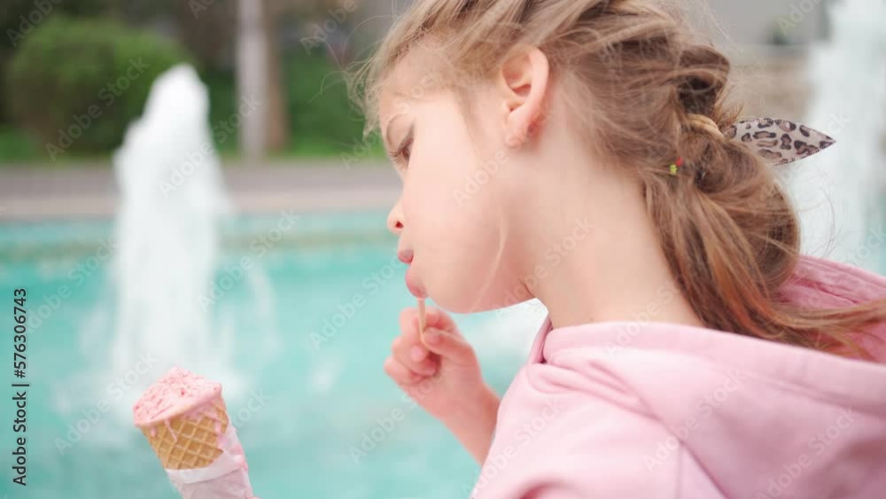 Little Cute Up Girl with Make in Pink Hoodie Enjoying Delicious Ice Cream. Kid with Ice Cream in the City Park Sitting near Fountain. Enjoy Summer and Childhood Little Cute Up Girl with Make in Pink Hoodie Enjoying Delicious Ice Cream. Kid with Ice Cream in the City Park Sitting near Fountain. Enjoy Summer and Childhood