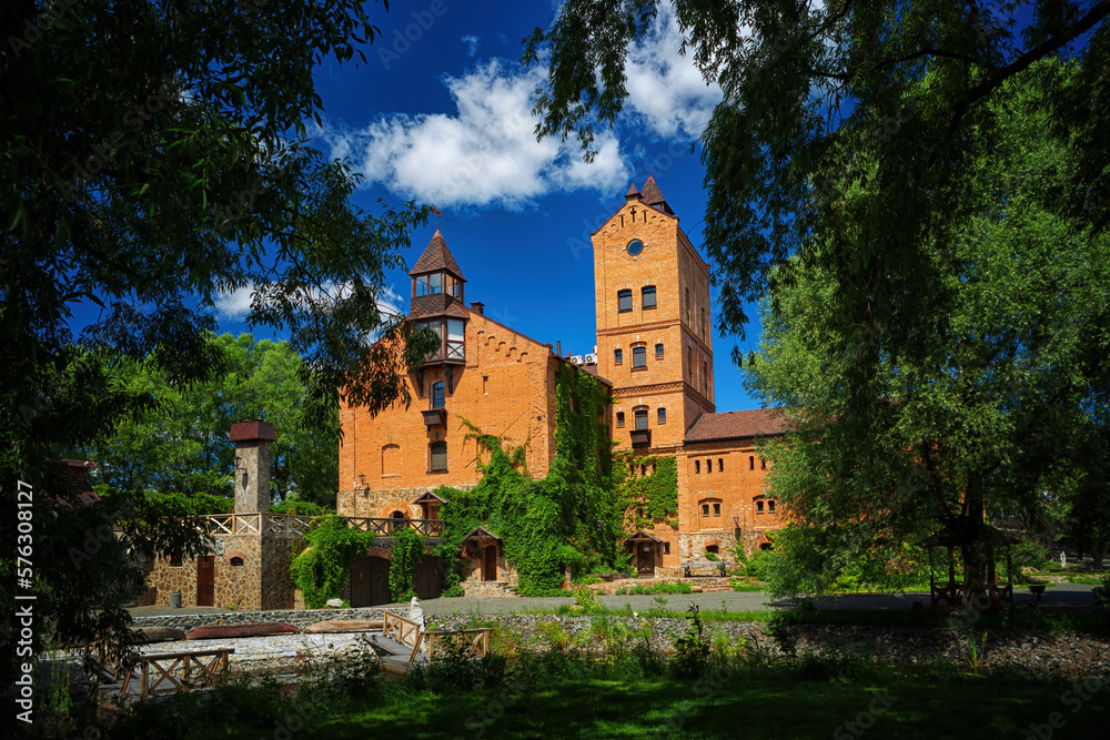 Fototapeta premium Ancient castle green trees against a background of blue sky and white clouds