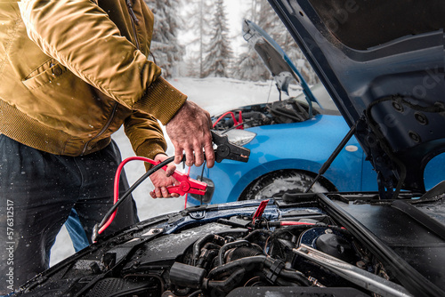 Automobile starter battery problem in winter cold weather conditions. mechanic using jumper cables to start-up a car engine. Low battery. 