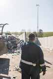 Landfill worker directing skid steer loader on the garbage heap. Waste disposal, consolidation, and transfer concept.