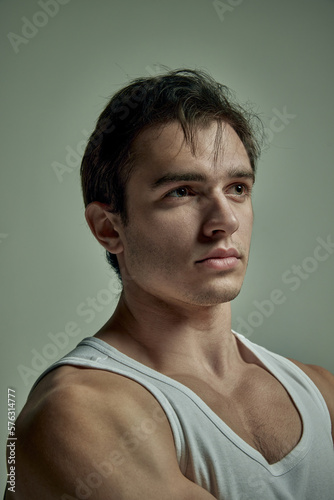 Portrait of serious handsome young man with muscular body posing in singlet over pale green studio background. Concept of man's beauty, sportive and healthy lifestyle, fashion
