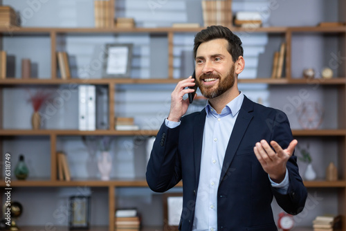 Photographie Mature successful boss happy with achievement talking on phone inside office, senior lawyer consulting clients on phone, businessman wearing glasses in business suit, man at workplace standing