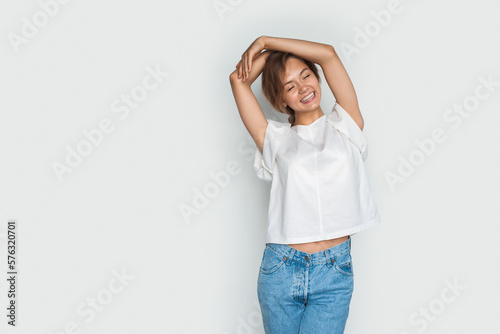 Attractive young woman relax posing with her hands over her head and eyes closed on a white studio background with copy space.