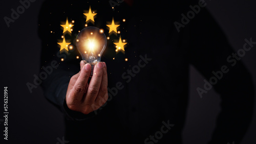 businessman holding a light bulb concept of global business to driven startup with five stars success. Bright lights give hope to small businesses. invention, finance, Copy space, black background