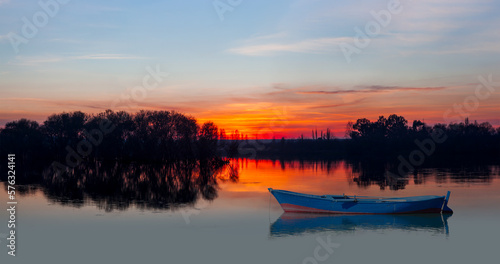 Silhouette of birds flying over the lake in the foreground blue boat at sunset © muratart