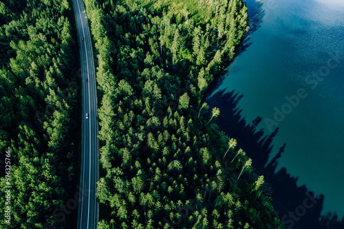 Aerial view road through green woods and blue lake in Finland.