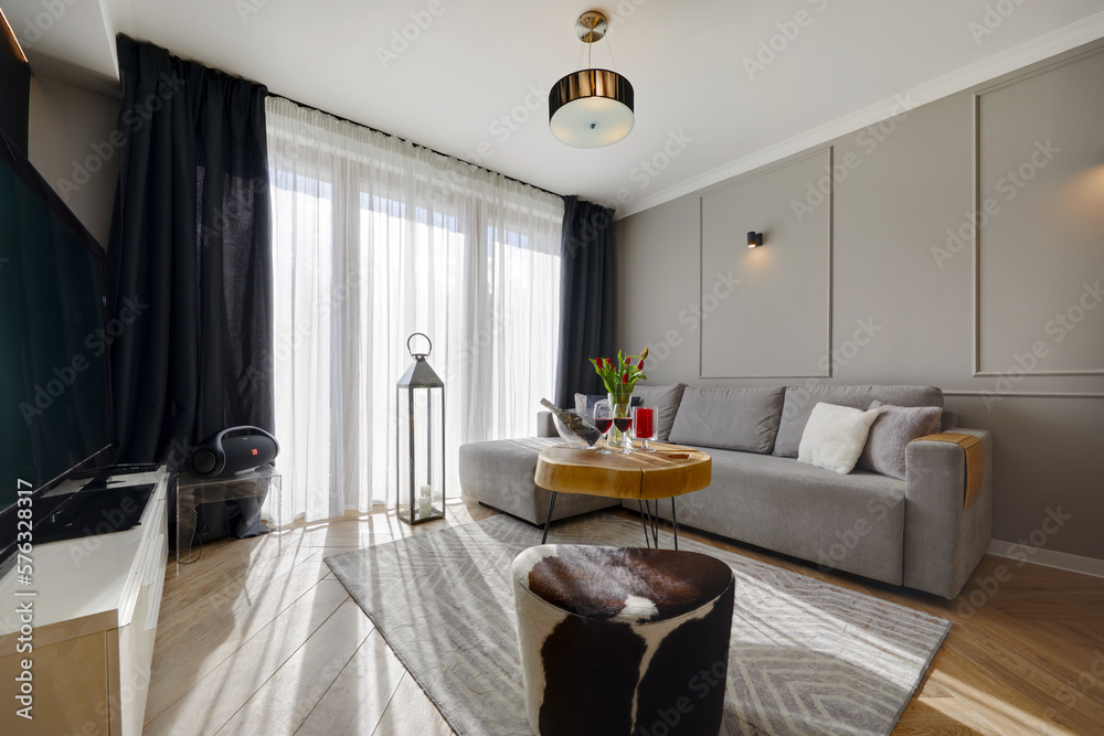 Fototapeta premium Przytulny apartament z wygidą sofą, na pierwszysm planie stolik kawowy z butelką wina i kieliszkami