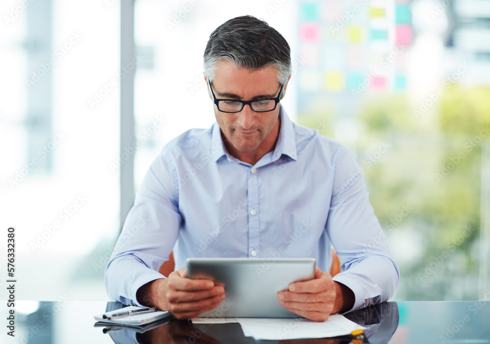 Connected to the corporate world. Cropped shot of a mature businessman working on his tablet in the office. Connected to the corporate world. Cropped shot of a mature businessman working on his tablet in the office.