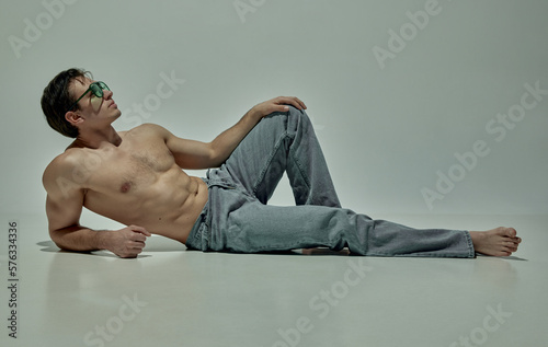 Handsome young man with strong muscular body shape posing shirtless in jeans over grey studio background. Concept of man's beauty, sportive and healthy lifestyle, fashion, strength photo