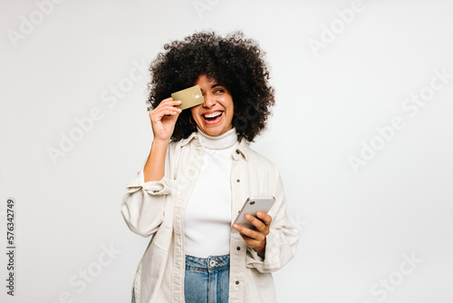 Cheerful young woman holding a credit card and a smartphone in a studio photo