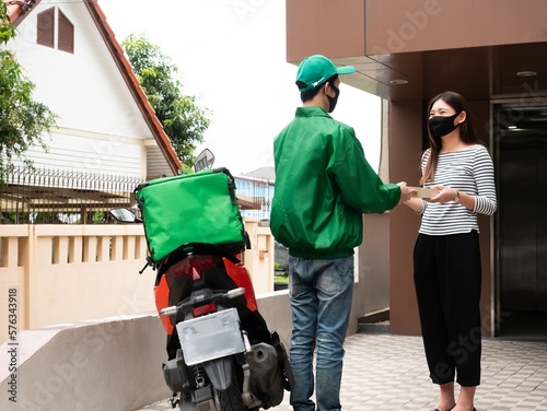 Fotografi Asian delivery man ride motorcycle and wear green uniform pick up food and deliv