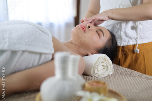 Relaxed Asian woman receiving beauty massage in spa salon.