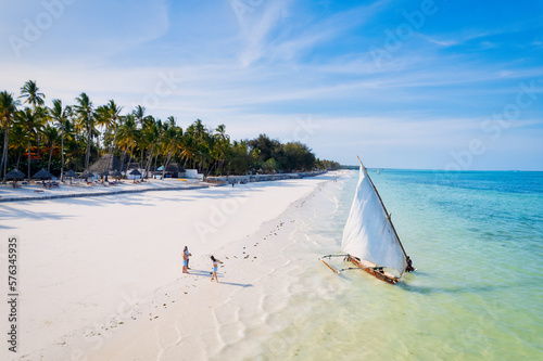 Relax on the white sand beach in Kiwengwa village on Zanzibar while admiring a Dhow catamaran sailboat gently gliding through the crystal-clear waters. photo