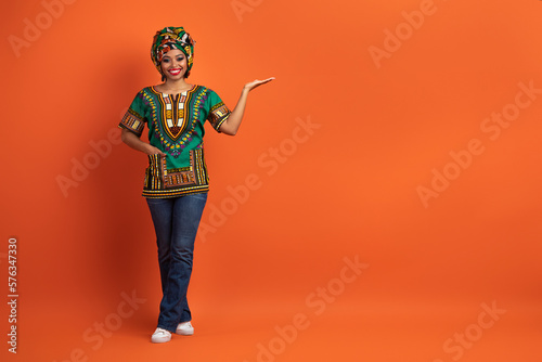Attractive black lady in colorful outwear pointing at copy space