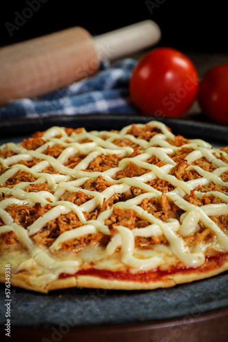 Chicken pizza with creamy cheese (catupiry) with tomatoes and a rolling pin in the background