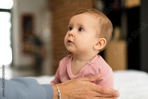 Childcare concept. Cute little baby girl sitting on bed and looking at mom, relaxing together in bedroom, copy space