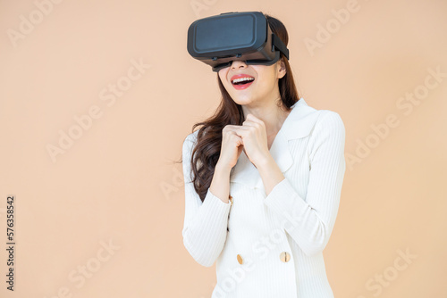 portrait of a young asia woman wearing a white cardigan and VR glasses. She is amazed by what she is seeing. Virtual reality headset. isolated orange background