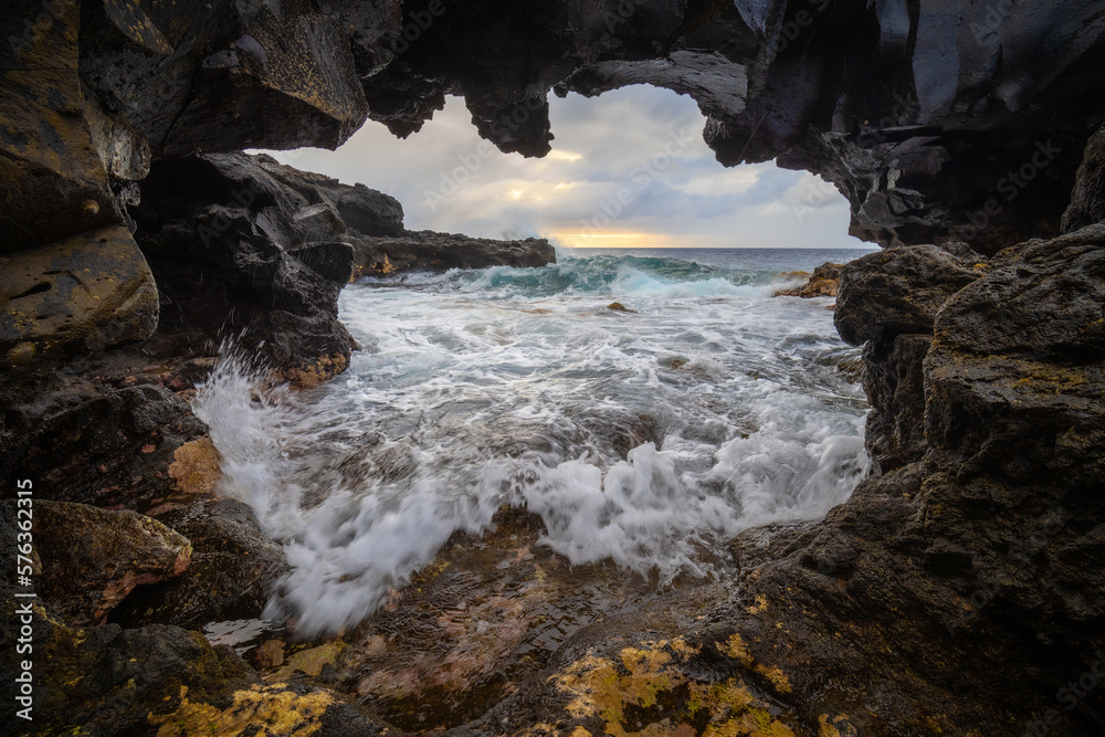 a view of the stormy sea through a view through a lava rock at sunrise. West coast of the island of La Palma