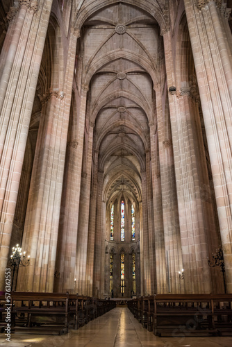 Central nave of the monastery with columns and arches, perspective from benches in lowlight to the chapel in the background, Batalha PORTUGAL