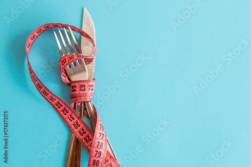 Foto Garfo e faca com fita métrica magenta ao redor, fundo azul dieta