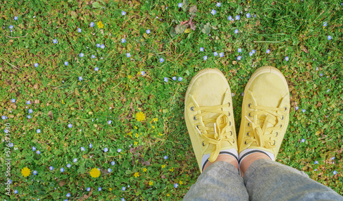 Yellow sneakers on a green spring meadow with yellow flowers, the beginning of spring and travel time. first person point of view, top view with copy space, idea for background or postcard