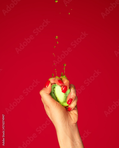 Fototapeta Naklejka Na Ścianę i Meble -  Ripe and juicy. Authentic female hand squeezes half of kiwi fruit over magenta background. Pop art food photography. Drops of juice fly up