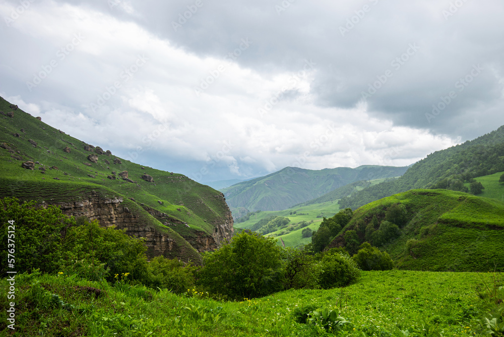 Amazing view of green mountains with clouds and dramatic sky. Majestic mountains and a beautiful green valley surrounded by forested mountains on a rainy spring day.