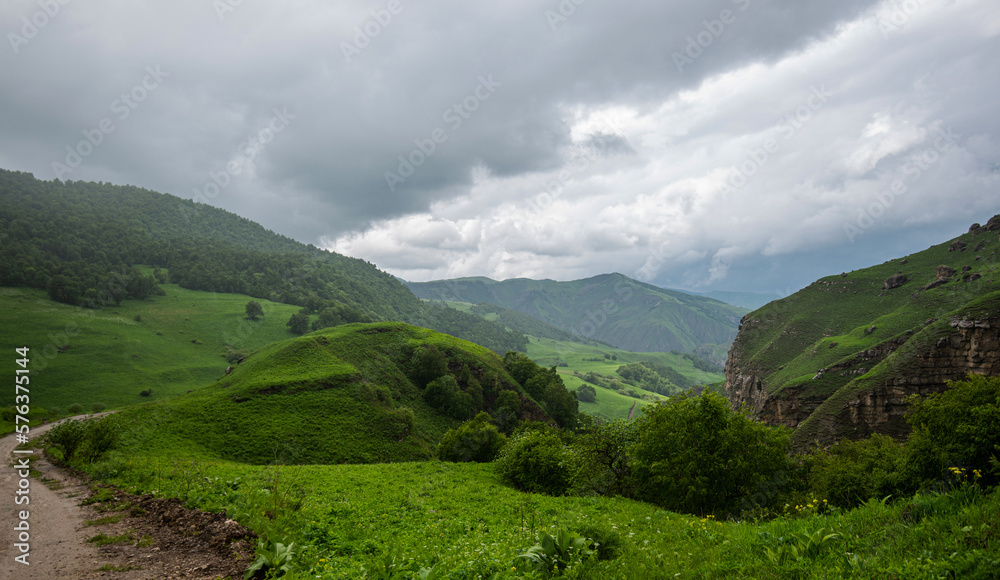 Amazing view of green mountains with clouds and dramatic sky. Majestic mountains and a beautiful green valley surrounded by forested mountains on a rainy spring day.