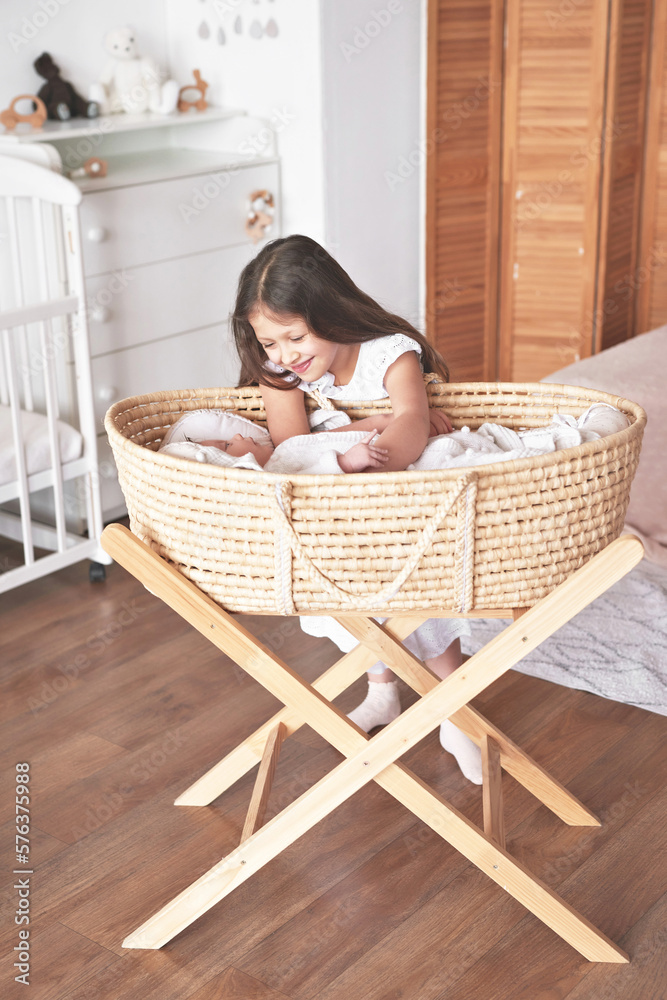 Sister and brother. Girl with baby boy in wicker cradle. Happy childhood. Children room Sister and brother. Girl with baby boy in wicker cradle. Happy childhood. Children room