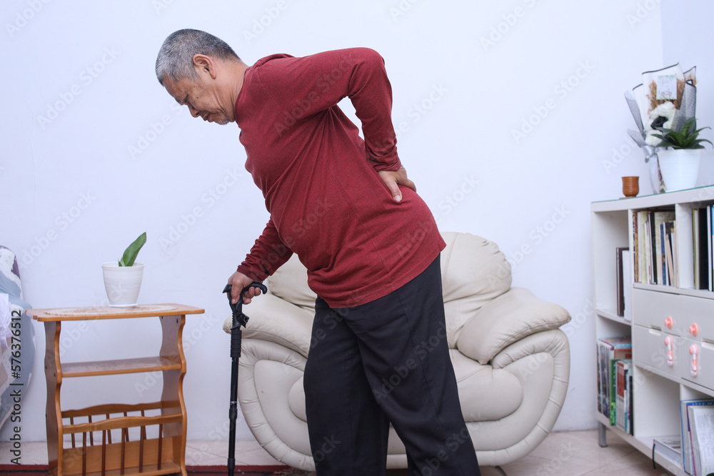 Senior asian man with walking stick suffering from pain in the back and waist at home Senior asian man with walking stick suffering from pain in the back and waist at home