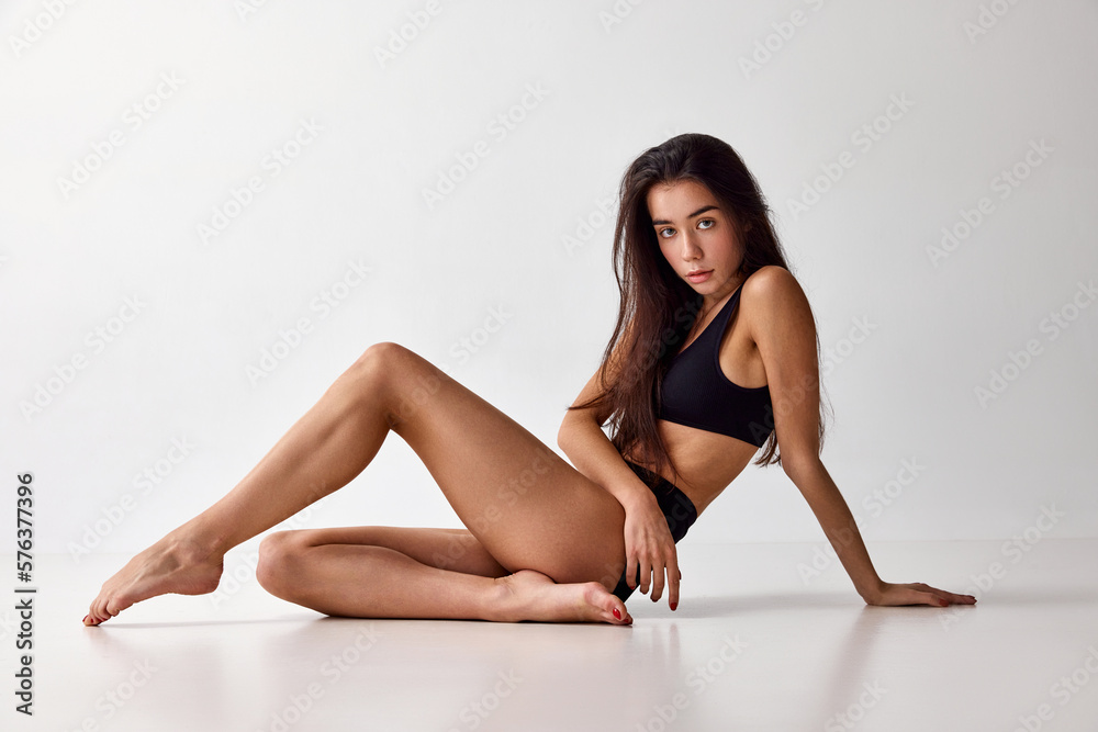 Portrait of beautiful young brunette girl with slim fit body posing in black underwear over grey studio background. Anti-cellulite care. Concept of natural beauty, spa, wellness, body care, fitness