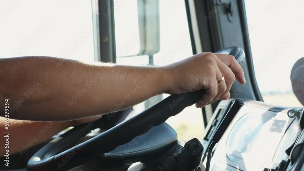 Male arms of lorry driver holds a big steering wheel while operating a truck at sunny day. Trucker riding to destination at country road. Concept of logistics and transportation. Close up Slow mo Male arms of lorry driver holds a big steering wheel while operating a truck at sunny day. Trucker riding to destination at country road. Concept of logistics and transportation. Close up Slow mo