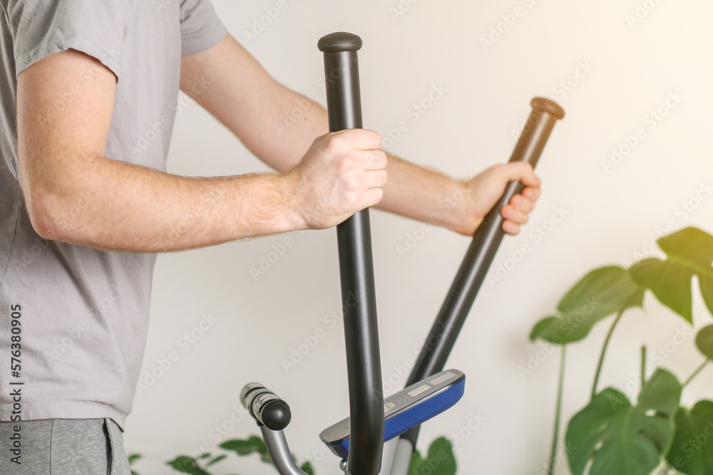 A man trains on an Elliptical Machine. Sports trainer at home in the apartment. Sports at home. A man trains on an Elliptical Machine. Sports trainer at home in the apartment. Sports at home.