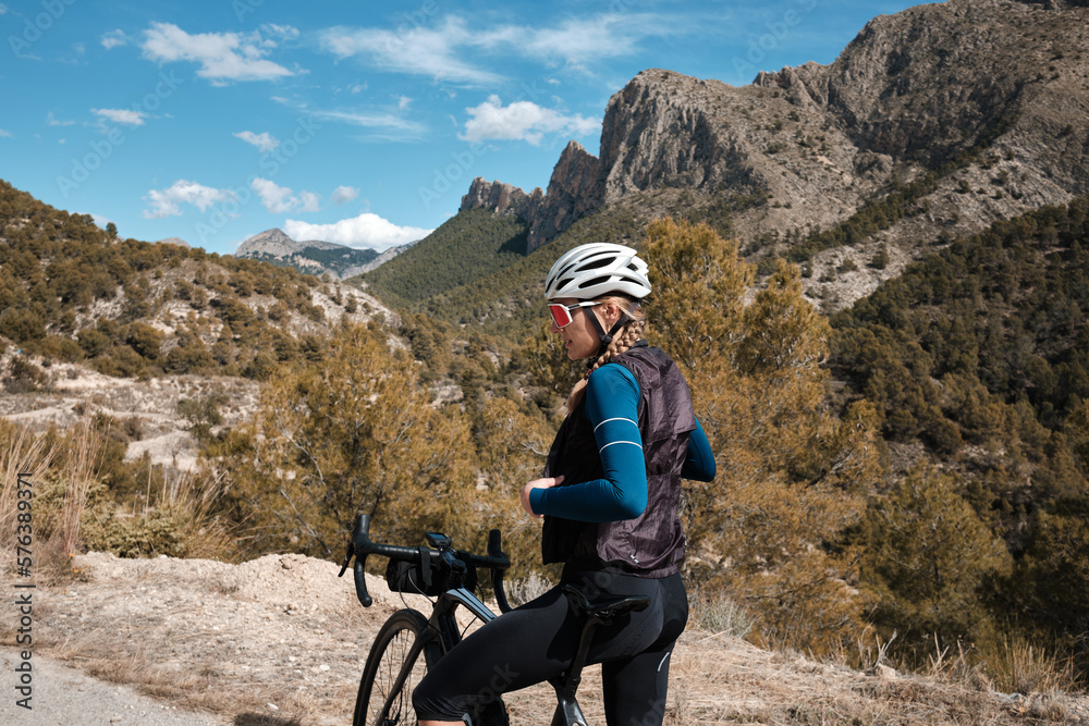 A female cyclist wearing cycling clothes and a helmet takes off her cycling vest after finishing her ride.Finestrat, Alicante, Spain A female cyclist wearing cycling clothes and a helmet takes off her cycling vest after finishing her ride.Finestrat, Alicante, Spain