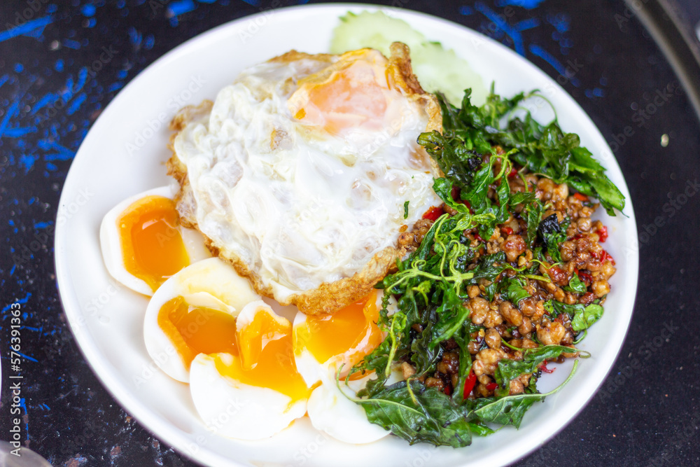 Rice with stir fried pork and basil with soft boiled egg and fried egg sliced cucumber on White Plate focus view Rice with stir fried pork and basil with soft boiled egg and fried egg sliced cucumber on White Plate focus view