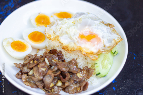 Rice with Fried Pork with Garlic with soft boiled egg  and fried egg sliced ​​cucumber on White Plate focus view