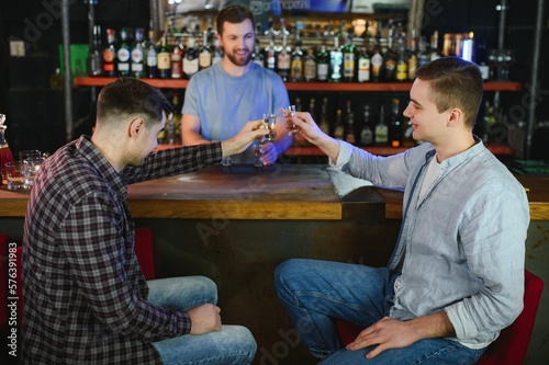 Barman pouring hard spirit into glasses for two male friends relaxing in a bar