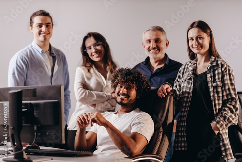 Friendly business team posing together near computer. Diverse coworkers smiling to camera. Group of colleagues having a good time