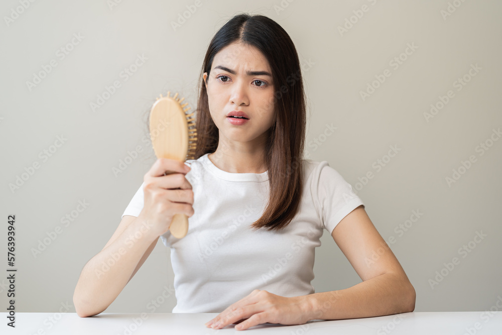 Serious asian young woman holding brush holding comb, hairbrush with fall black hair from scalp after brushing, looking on hand worry about balding. Health care, beauty treatment, hair loss problem. Serious asian young woman holding brush holding comb, hairbrush with fall black hair from scalp after brushing, looking on hand worry about balding. Health care, beauty treatment, hair loss problem.