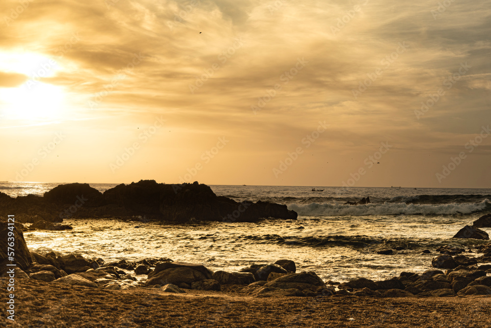 Obraz premium Golden sky among the clouds in the winter evening on a beach with rocks in Porto - Portugal