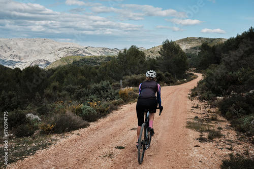 A woman cyclist is riding against a mountainous background.Female cyclist is riding a gravel bike on a gravel road.Cycling adventure. Parcent, Alicante, Spain