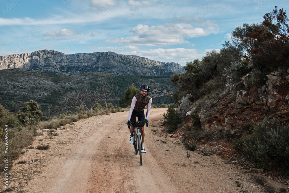 Fit male cyclist is riding dirt trails on a gravel bike. A man riding a gravel bike on a gravel road in a scenic view with hills in Castell de Castells,Alicante region, Spain. 
