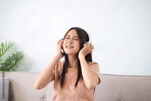 Young asian woman with headphones relaxing at home. listening to music. man sitting on cozy sofa wearing headphone