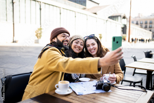 group of three happy friends taking selfie in outdoor cafe on sunny day - cheerful holidays concept