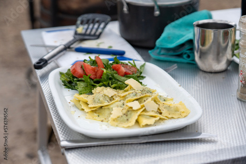 Ravioli with parmesan and a tomato salad on the side with greens on a camping table 