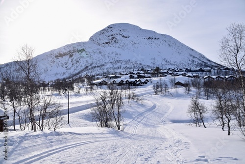 Snowy scenes in Hovden, Norway. Ski tracks on the ground, with Mountains and trees behind. Snow covered houses and blue skies. Bluebird weather.  photo