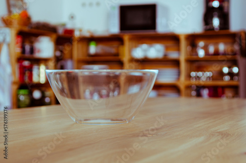 An empty glass bowl stands on a wooden table against a wooden kitchen background