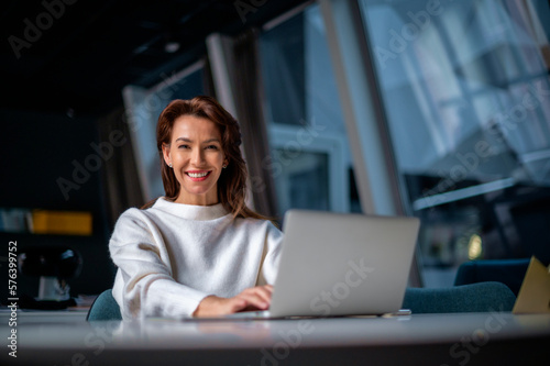 Brunette haired middle aged businesswoman sitting at the office and using laptop for work