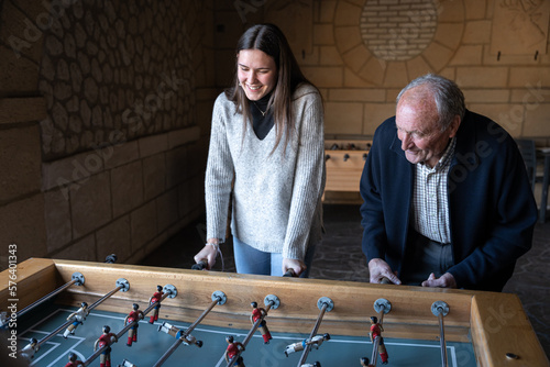 A granddaugther and his grandfather are playing table football game and having fun together photo